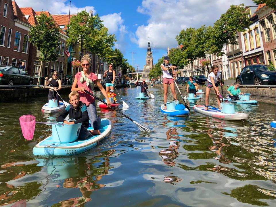 Mensen en kinderen op sups met bakken en schepnetten in Alkmaarse grachten